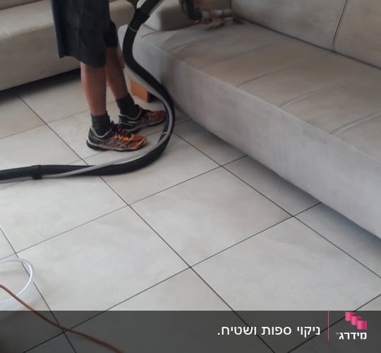אדם מנקה ספה עם שואב אבק מקצועי